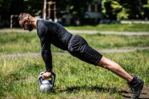 Outdoor exercising. Male athlete exercising with kettlebell in the park.