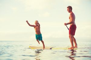Father and son stand up paddling at sunrise, Summer fun outdoor lifestyle